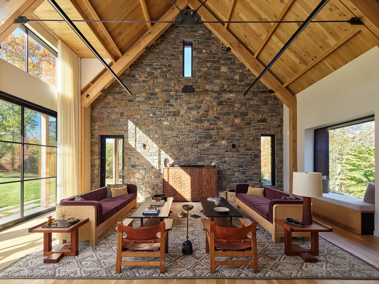 Living room features a vaulted wood ceiling, a stone wall with narrow vertical window, and large black-framed windows with a built-in window seat.