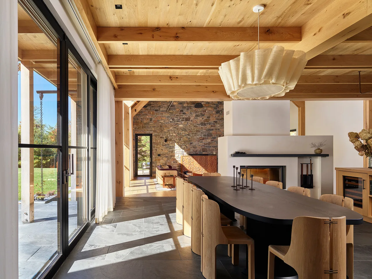 Dining room features a large black table, natural wood chairs, exposed wood ceiling with beams, and a white fireplace with stone accent wall beyond.