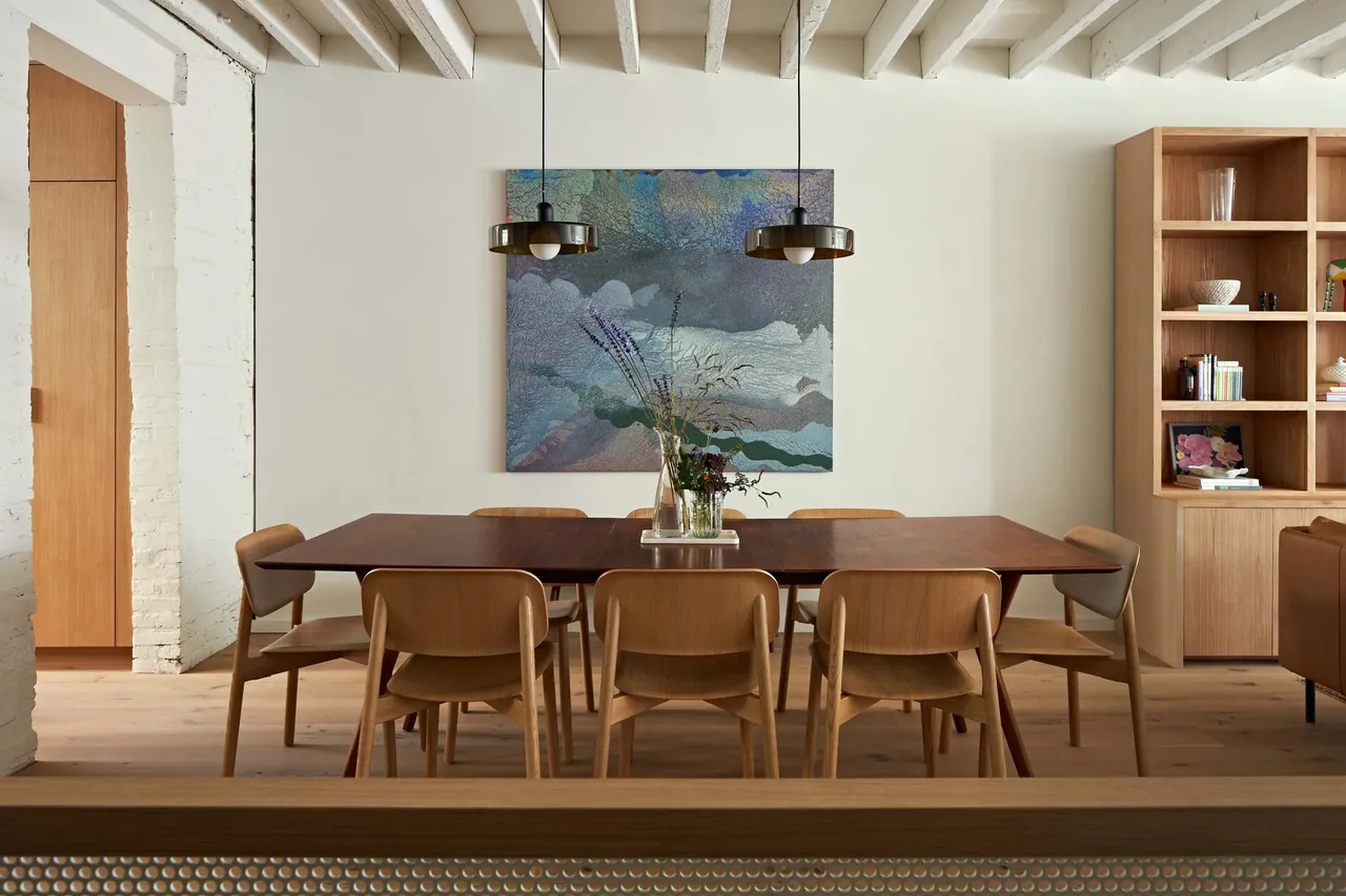 Dining space of Two Door House features a dark wood table, wooden chairs, pendant lighting, and built-in shelving.