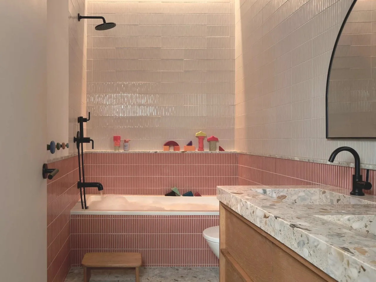 Bathroom features vertical pink and white tiles, a terrazzo double vanity, and black shower fixtures.
