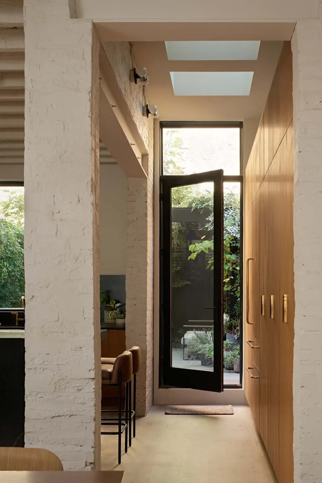 Interior hallway features wood cabinetry and a glass door leading to the garden with natural light from skylights above.