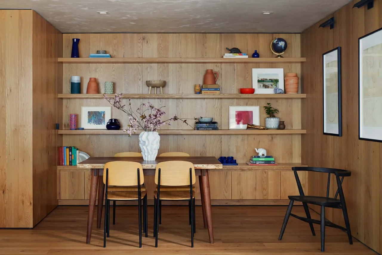 Dining room with natural wood built-in shelving and furniture accented by decorative objects and framed art.