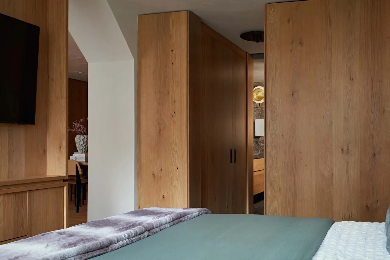 The bedroom features extensive wood paneling and opens to a bathroom with dark stone walls and a brass sconce.