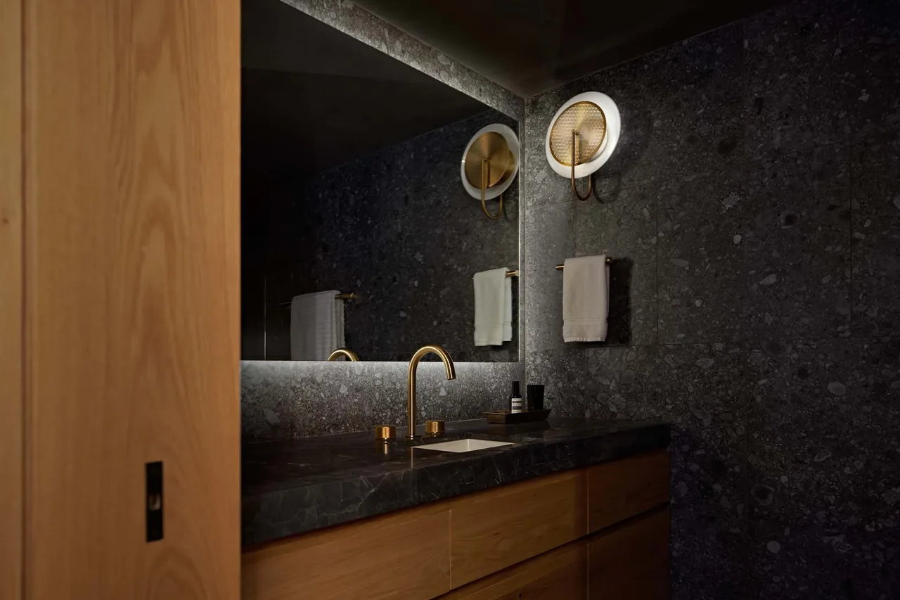Bathroom in The Low Penthouse with dark stone walls, a black stone countertop, brass fixtures, and a wood vanity.