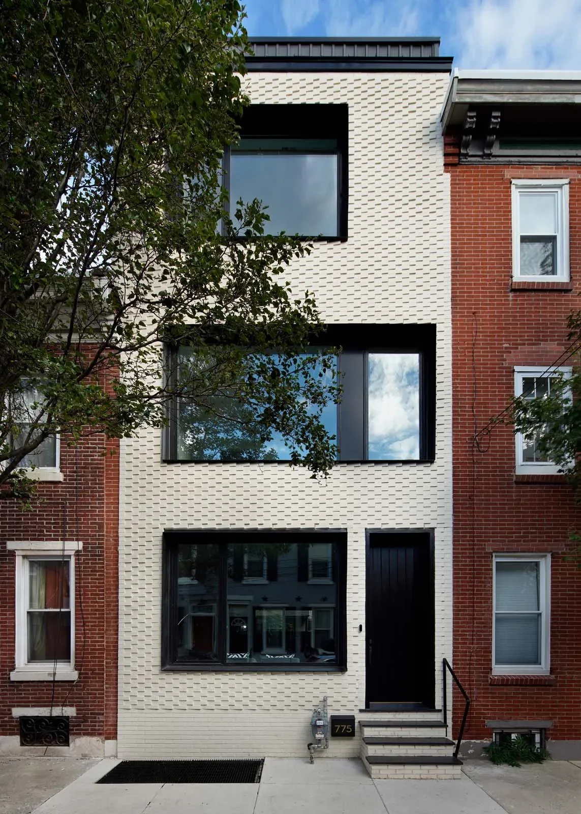 The Contextual House features a white textured brick facade with large black-framed windows and a black entrance door.