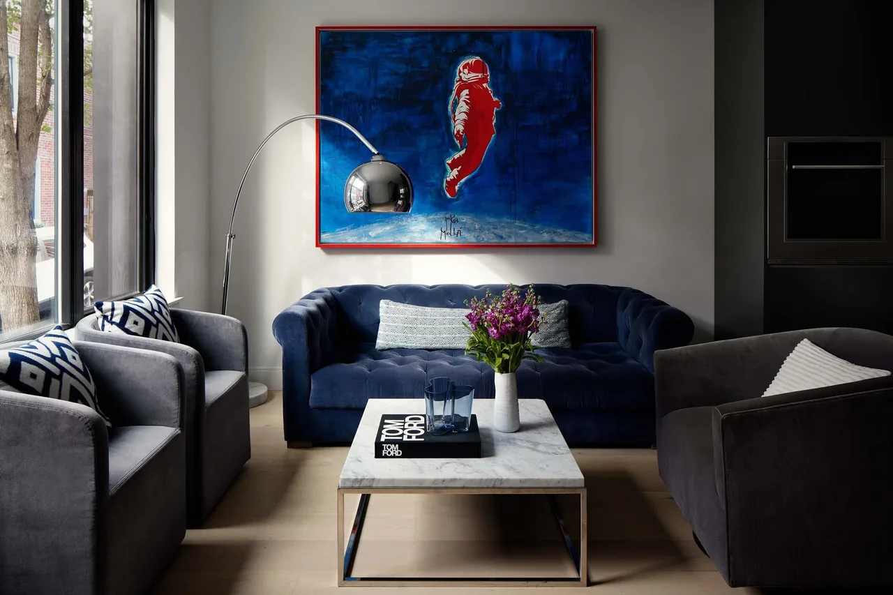 This living room features a blue velvet sofa, gray armchairs, a marble coffee table, and a large blue and red wall painting.