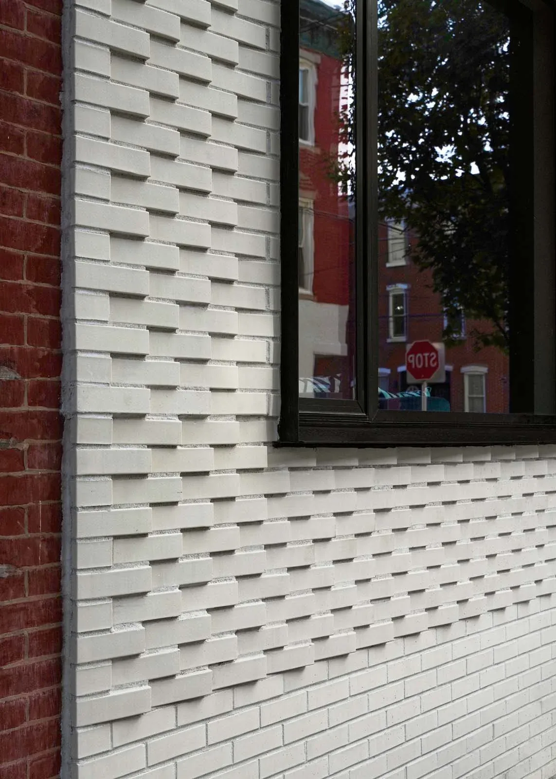 The Contextual House features a textured white brick facade with a black framed window reflecting the surroundings.