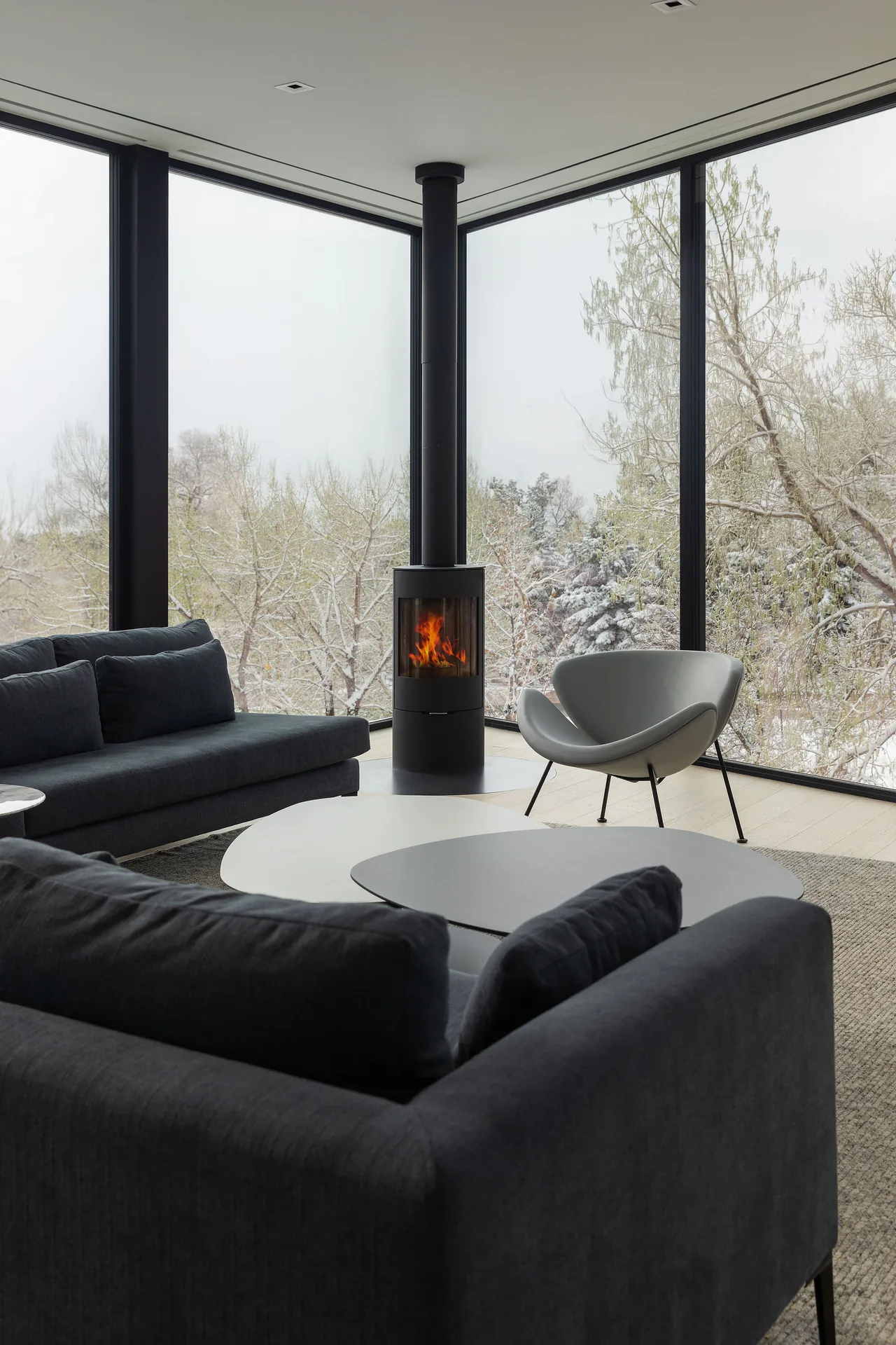 Spring Valley living room with black-framed floor-to-ceiling corner windows and a freestanding cylindrical fireplace.