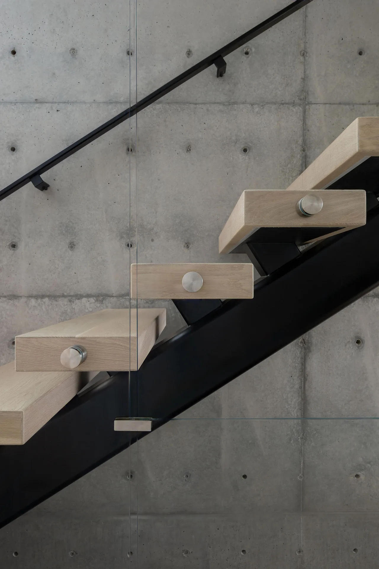 Floating wood stairs with a black metal frame and concrete wall backdrop in an interior space.