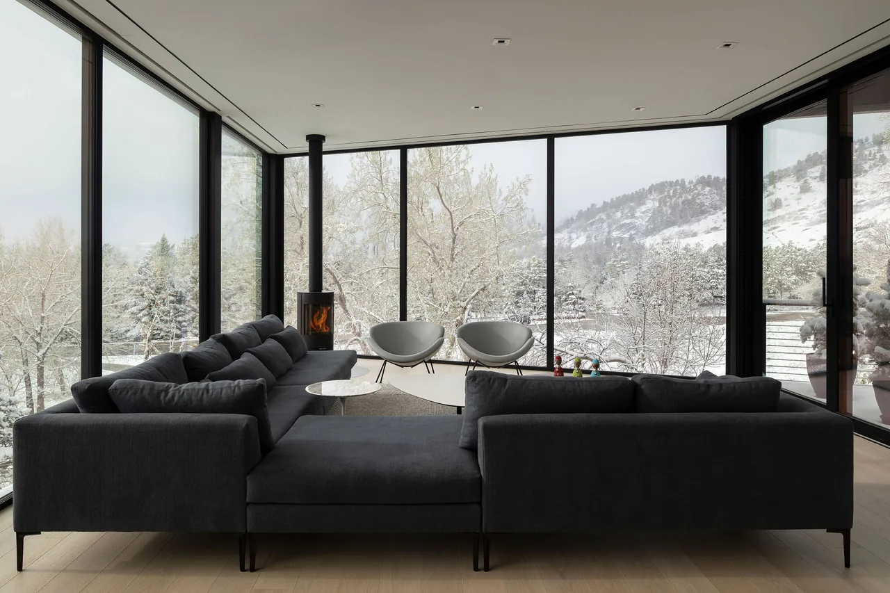 Living room of Spring Valley project with floor-to-ceiling windows and a wood-burning stove showing mountain views in winter.