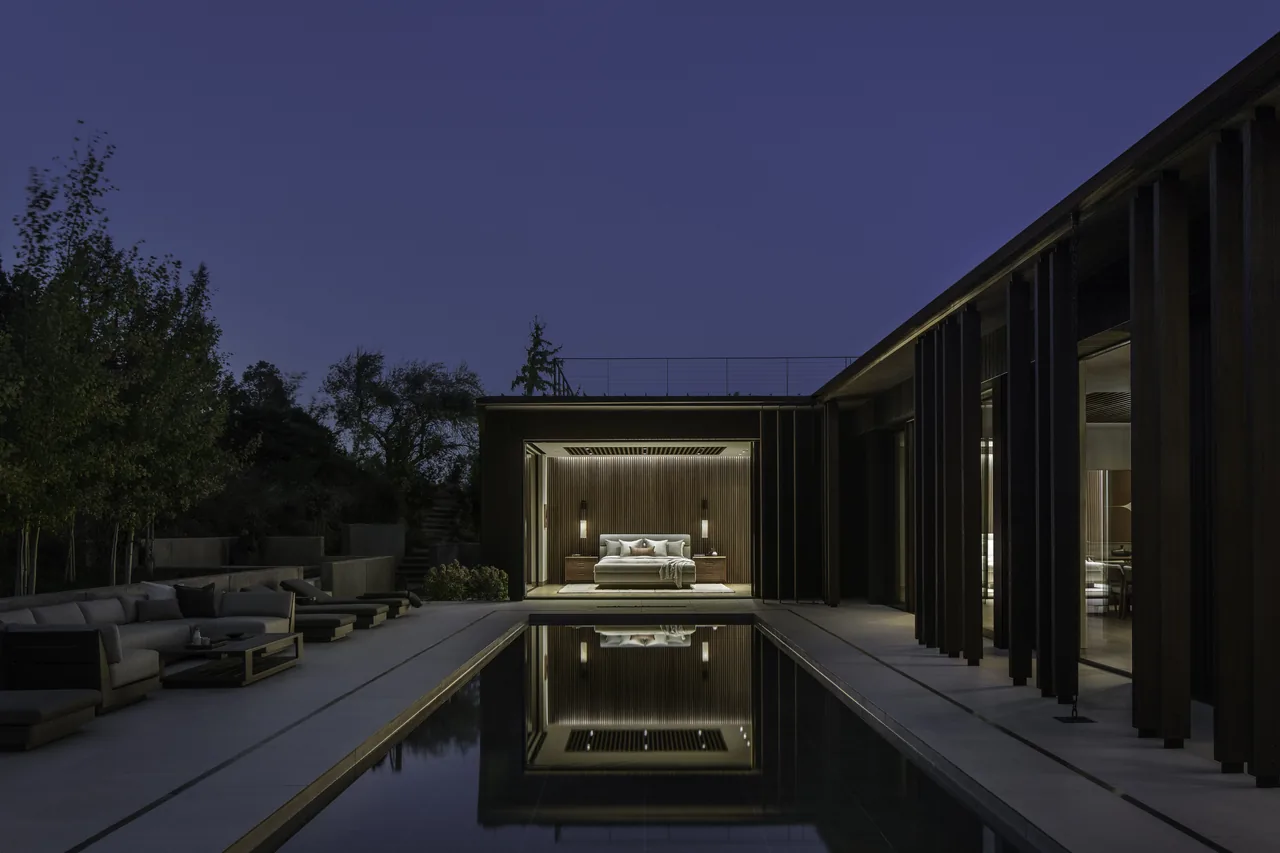 Panorama House features a nighttime view of its illuminated bedroom opening to a central pool and outdoor seating area.