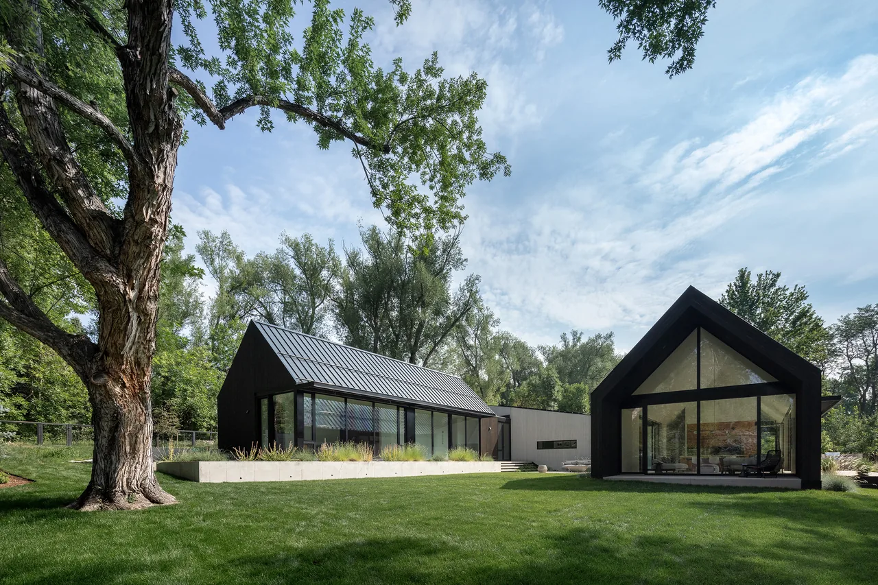 Two black-painted gabled structures with extensive glazing occupy a green lawn, featuring large triangular window panels and standing seam metal roofs.