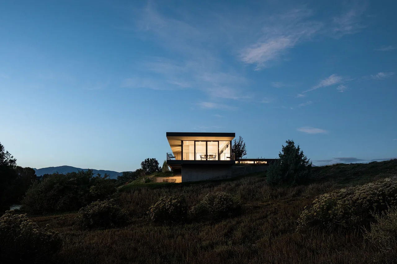 Rivers Edge project by Piché Architecture features a modern house perched on a hill with large windows and mountain views at dusk.