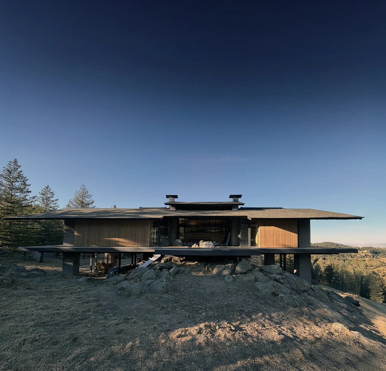 Sentinel Rock house by Piché Architecture features a wide flat roof and wood siding on a rocky hillsite.