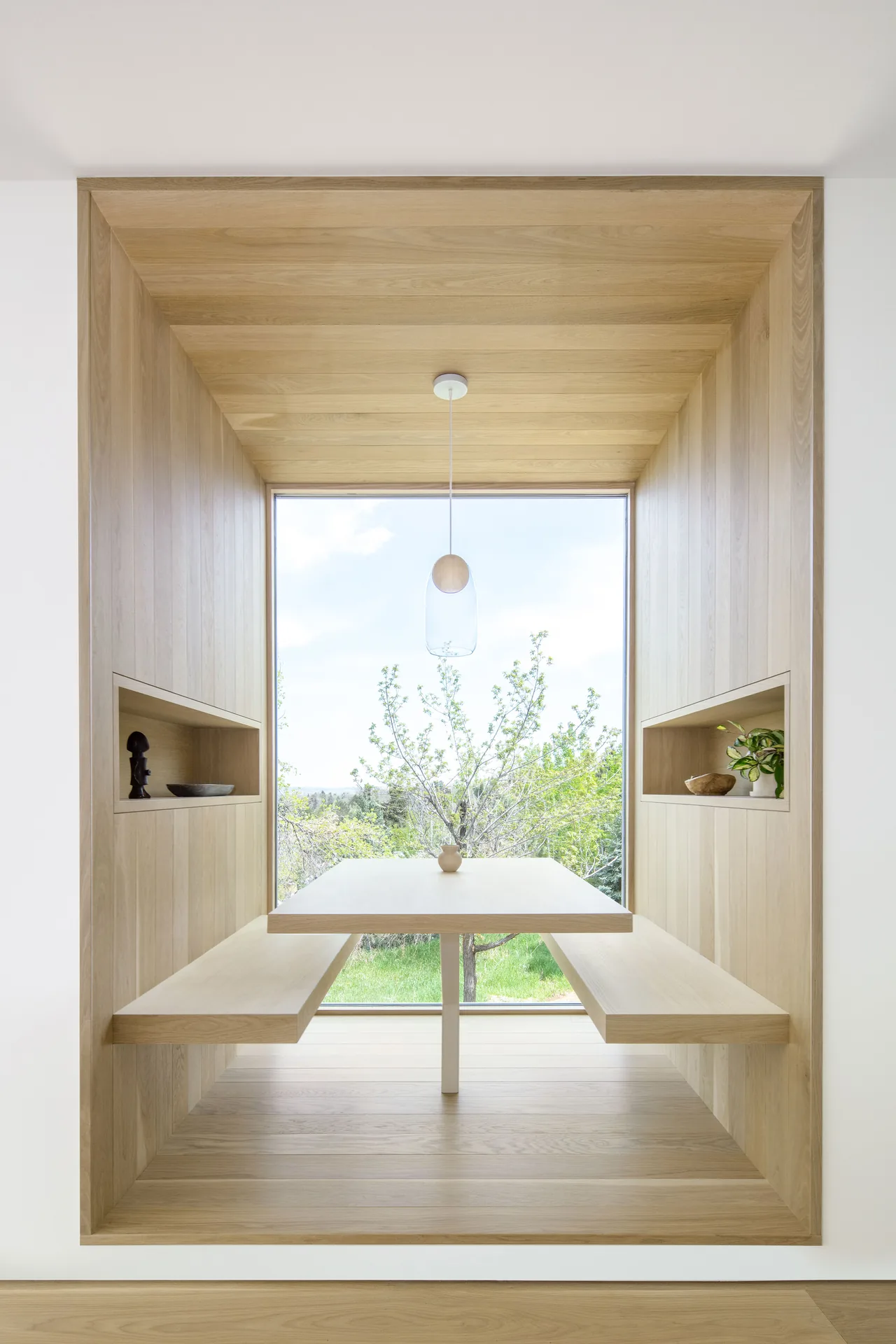 Dining nook in Villa H features built-in wood seating and table with large window view and wood paneling.