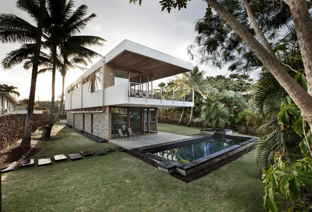 The Island House by Piché Architecture features a cantilevered second floor with balcony and a backyard pool surrounded by tropical landscaping.