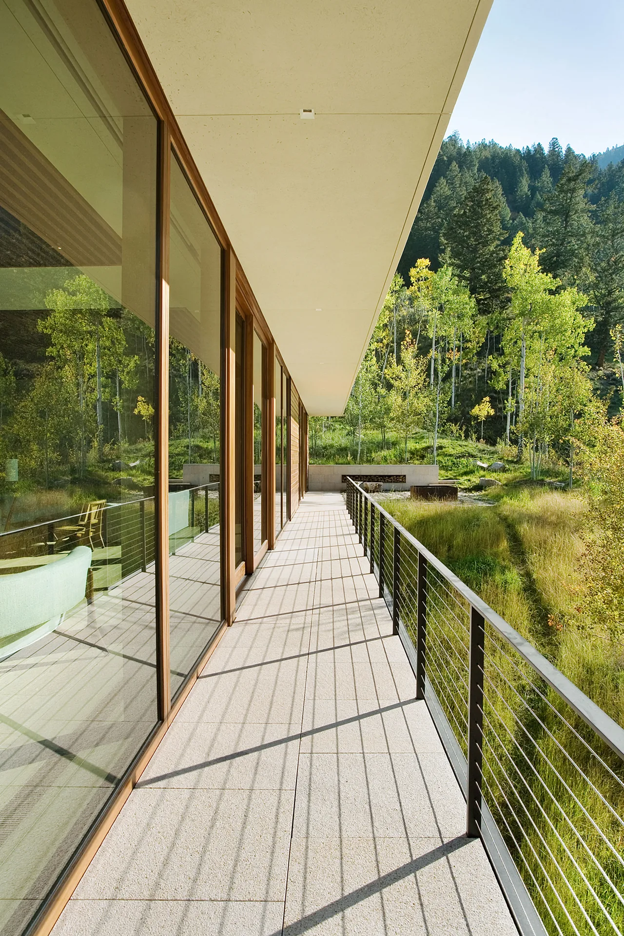 Linear House features a covered patio with floor-to-ceiling glazing and cable railing overlooking natural surroundings.