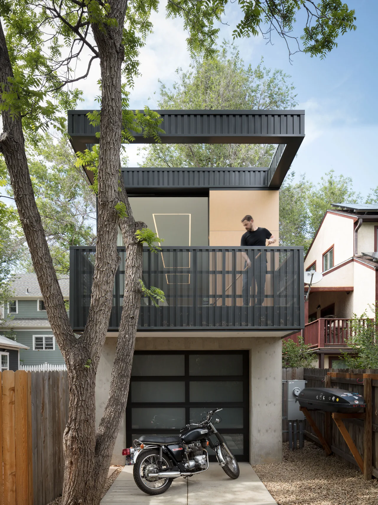 Two-story home with vertical black metal cladding, a glass garage door, and a balcony with perforated metal railing.