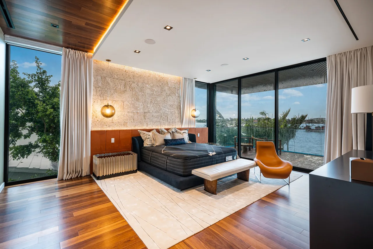 A bedroom featuring floor-to-ceiling windows, a wood-paneled ceiling, and a view of the waterfront.