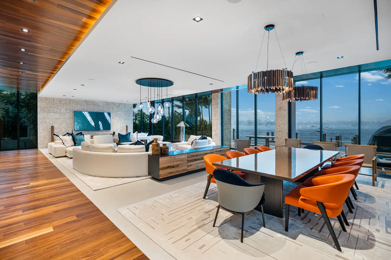 Open-plan living and dining area with floor-to-ceiling windows overlooks waterfront.