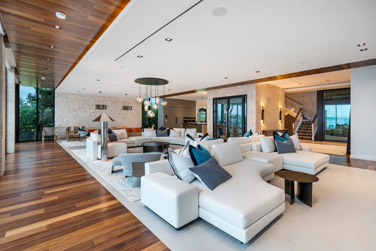 Open living room features white sectional sofas, wood flooring and ceiling, and a modern pendant light fixture above a lounge area.
