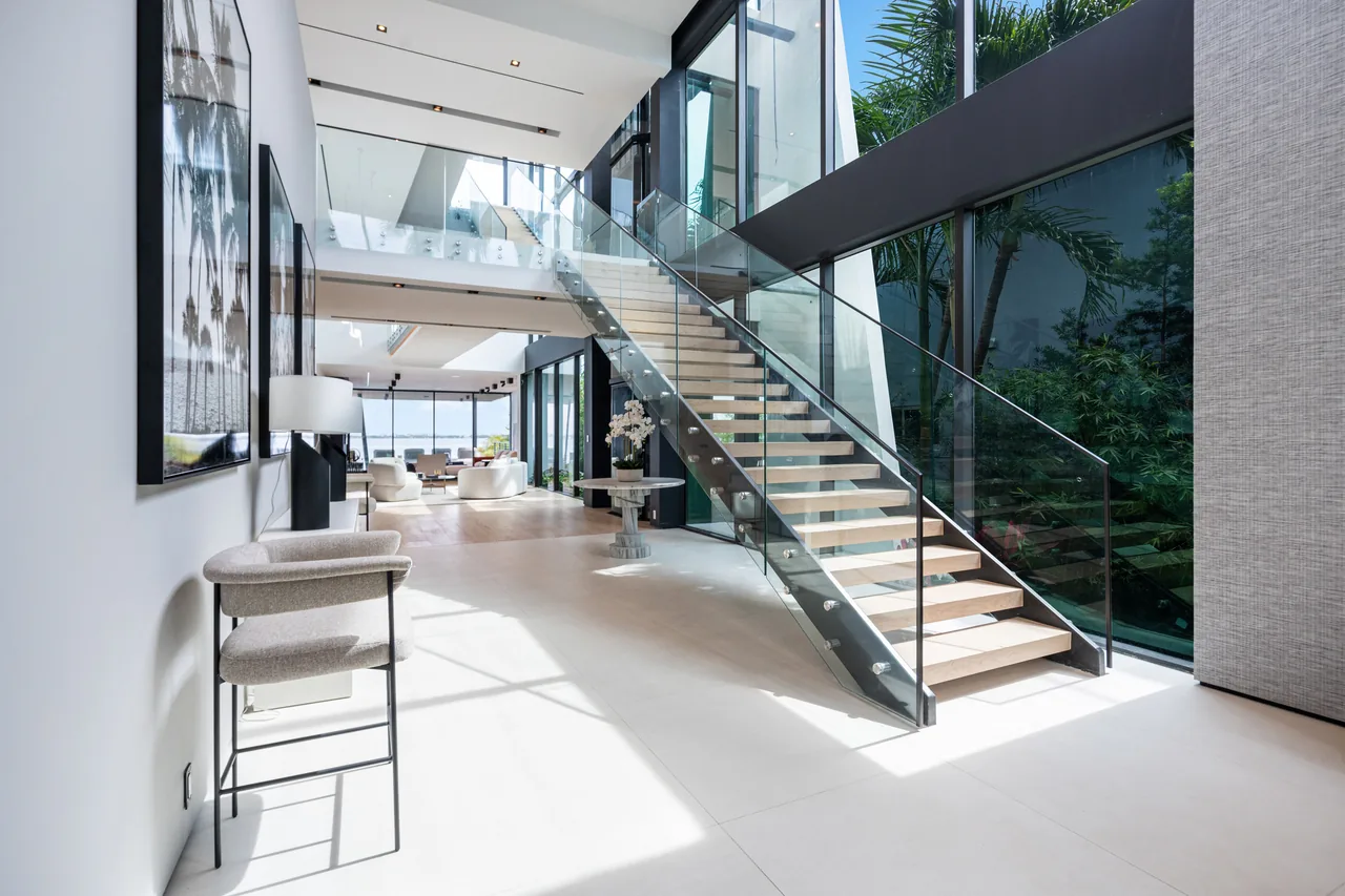 Modern interior featuring a floating staircase with glass guardrails and expansive windows overlooking lush greenery.