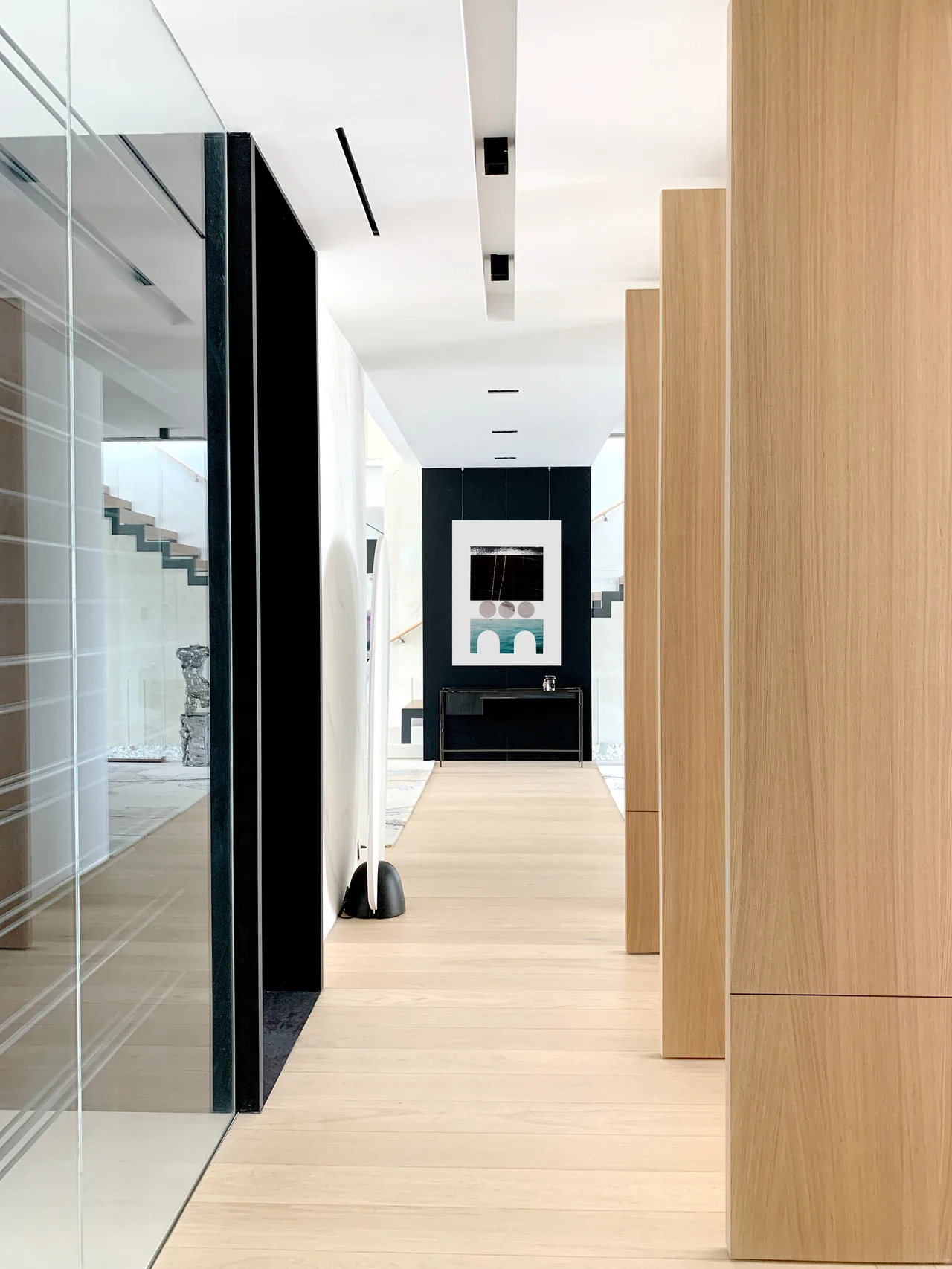 A modern hallway features light wood floors and vertical wood panels with a black framed abstract artwork at the far end.