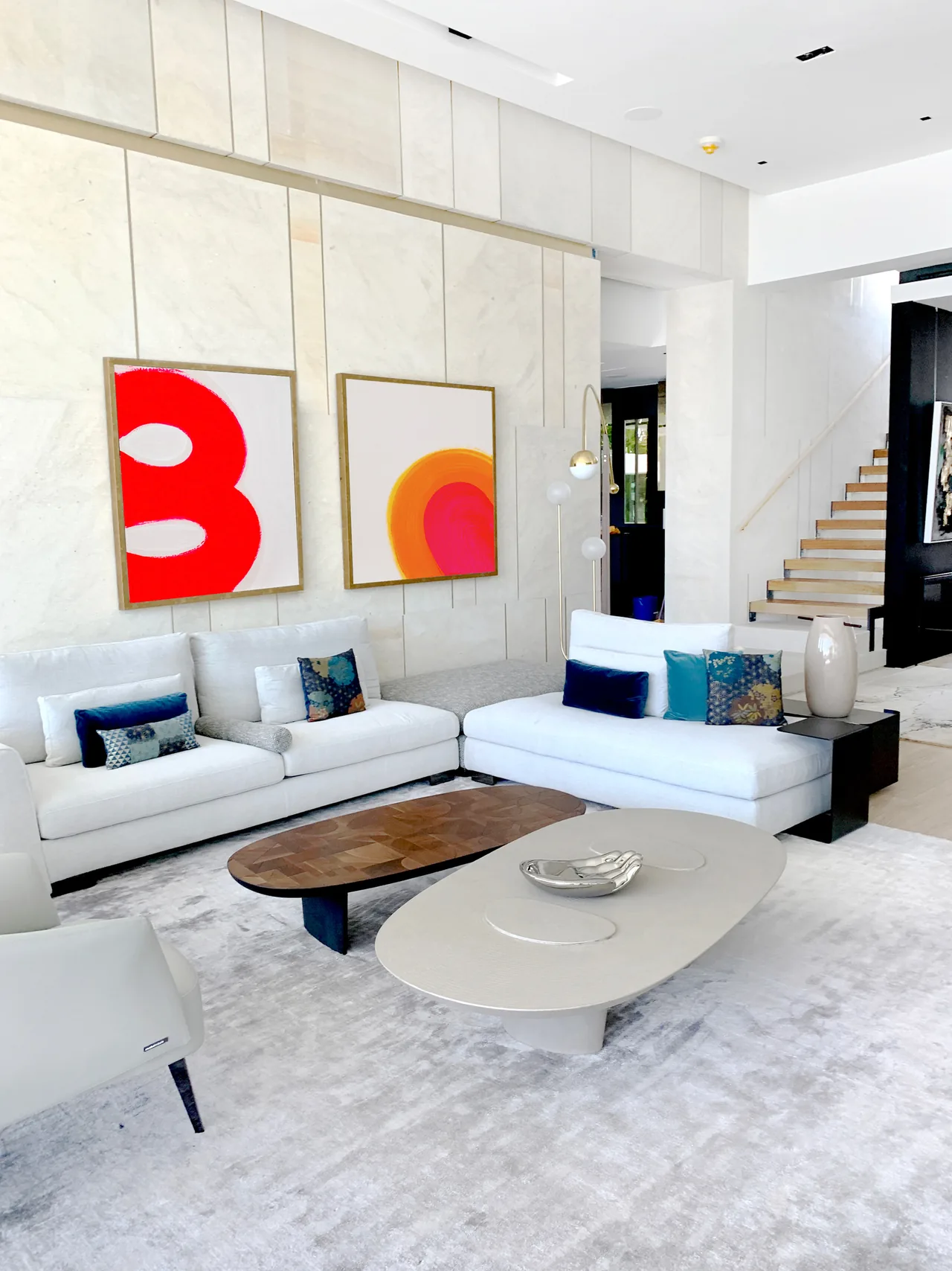 Living room features white sectional sofas, abstract wall art, and layered oval coffee tables with a neutral rug.