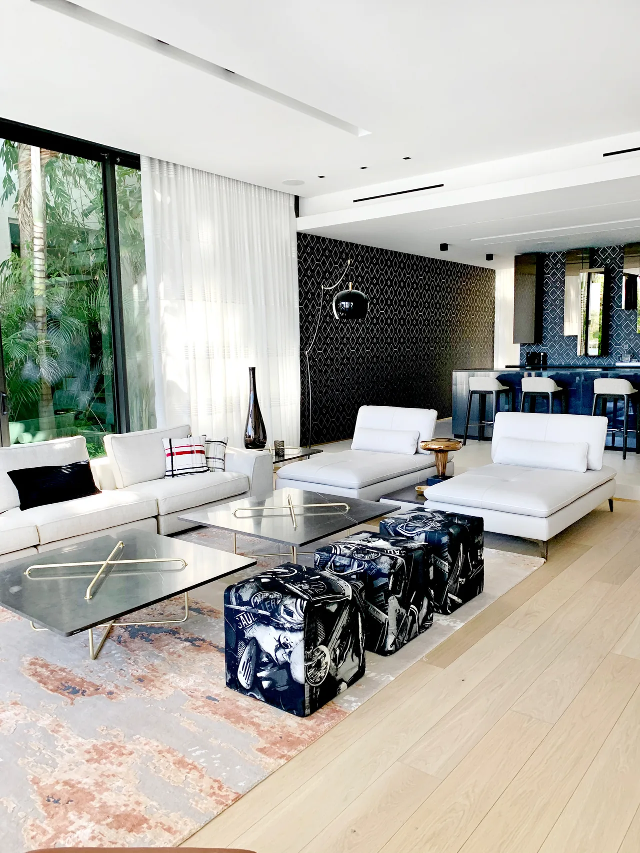 Living area in Palm Island Miami project features white sofas and artistic ottomans with a patterned black accent wall behind the bar.