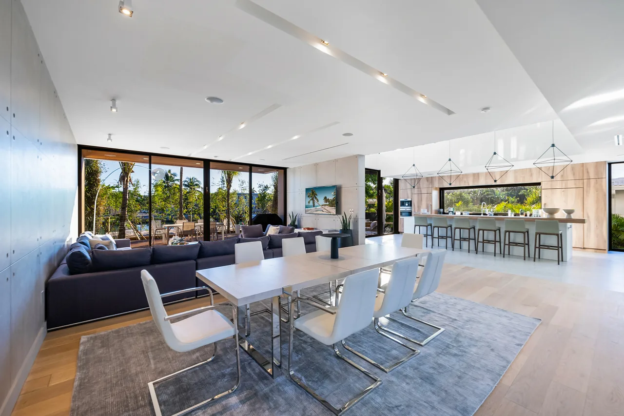 Modern open-concept dining and living room with floor-to-ceiling glazing and a view of the outdoor patio area.