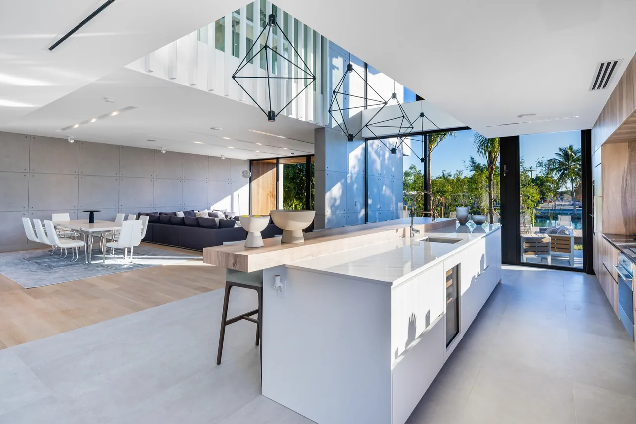Open-plan kitchen with a large island and dining table adjacent, featuring black window frames and geometric pendant lights.