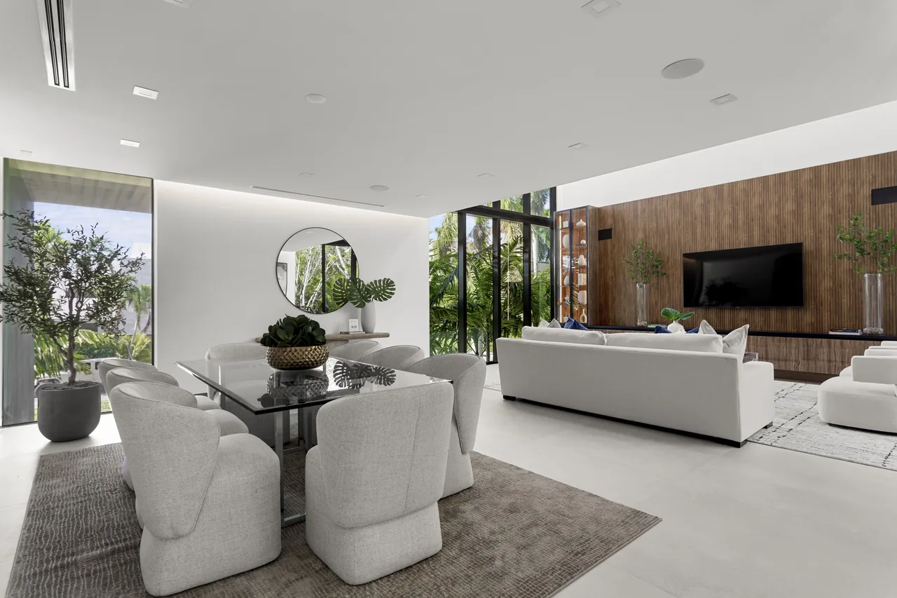 Open-plan living and dining room in the Fair Isle Residence featuring black window frames and a wood accent wall with a mounted TV.