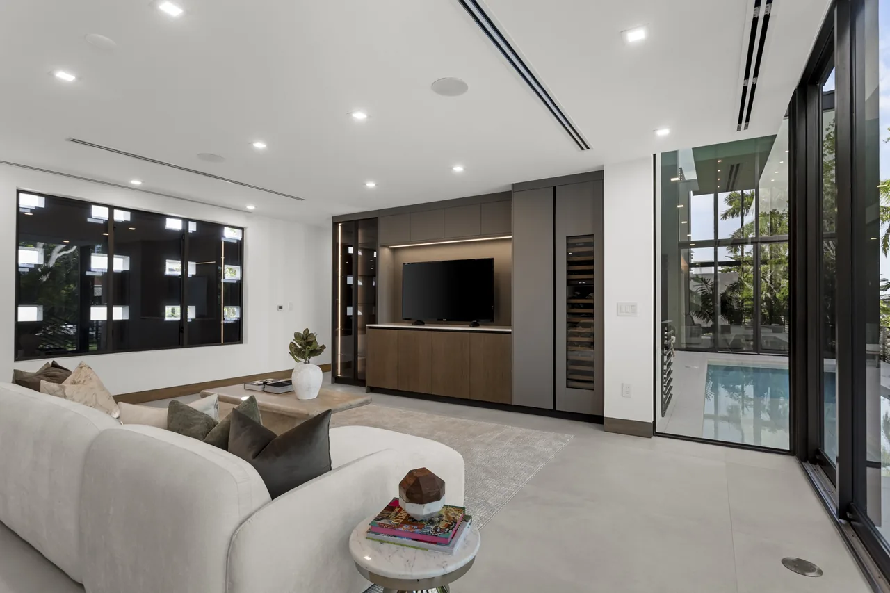 The Fair Isle Residence living room features clean lines, black-framed windows, and views of a rectangular pool outside.