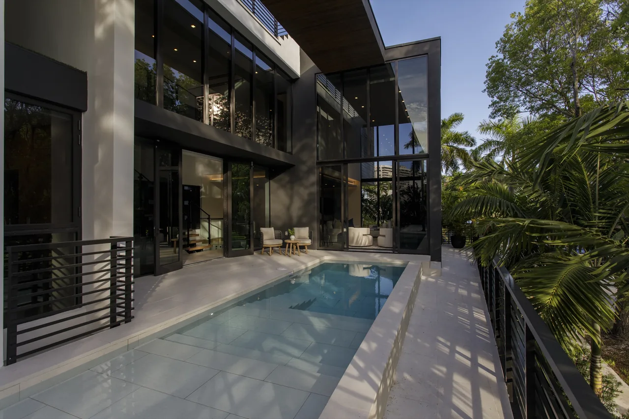The Fair Isle Residence features a modern exterior with floor-to-ceiling glazing and a rectangular pool adjacent to a patio seating area.