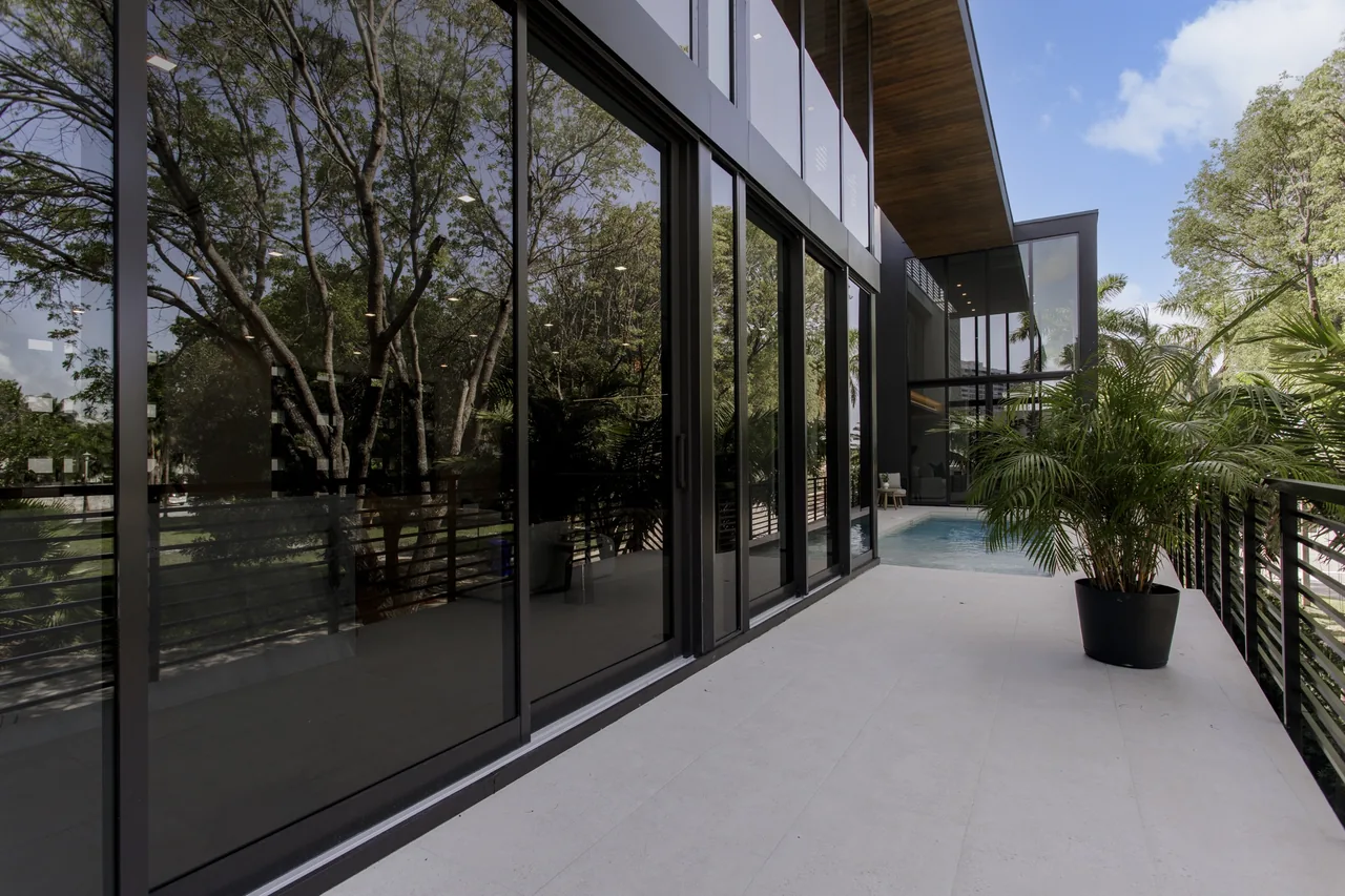 The Fair Isle Residence features an outdoor balcony with black window frames and a view of the rectangular pool and landscaped trees.
