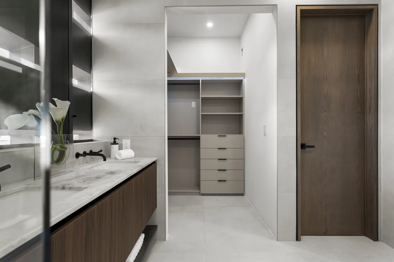 Bathroom with wood vanity, marble countertop, and adjacent built-in closet in the Fair Isle Residence.