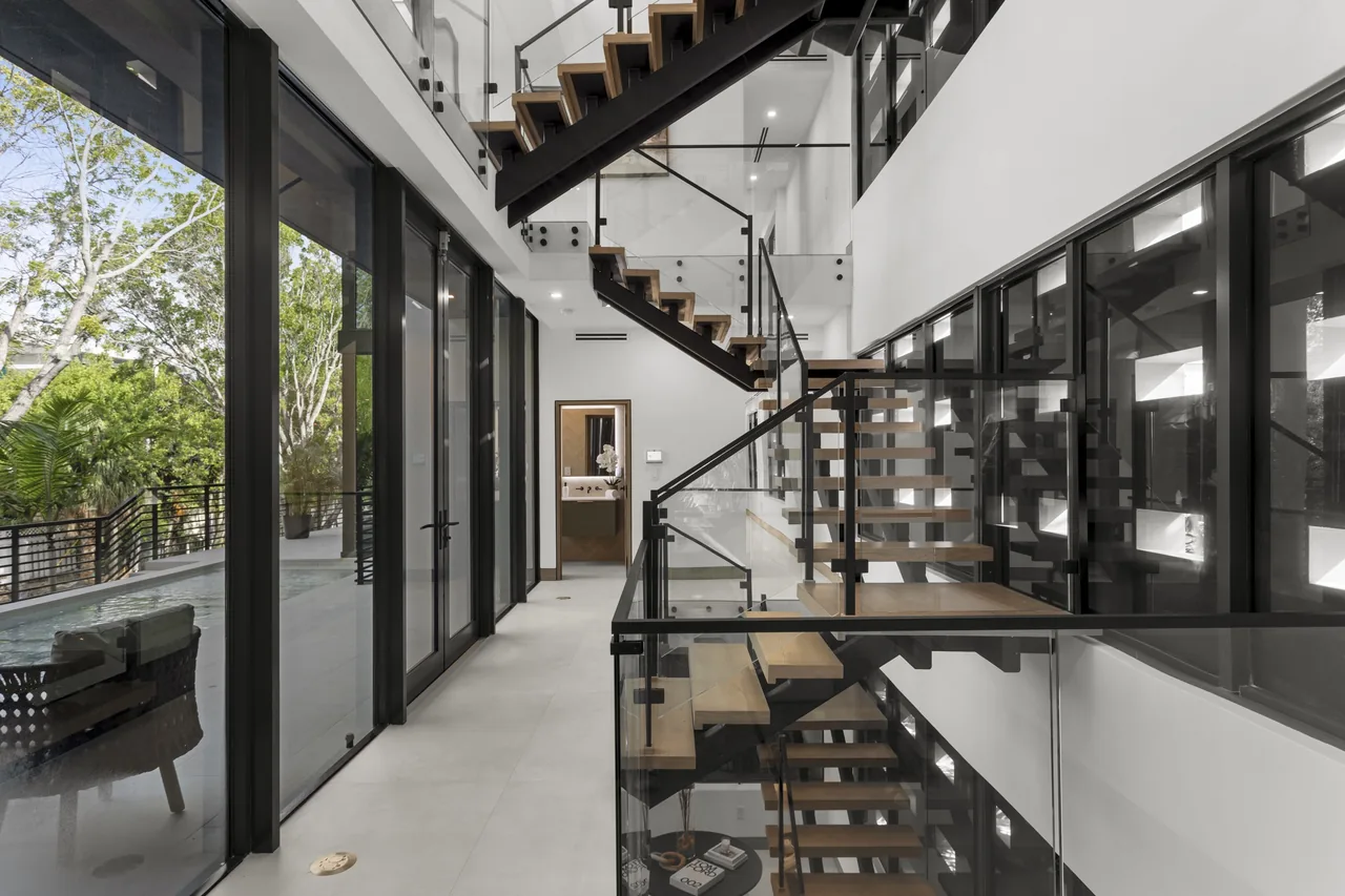 Modern stairwell with floating wooden stairs and floor-to-ceiling black-framed glazing at the Fair Isle Residence.