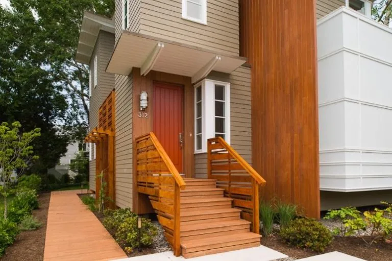 Prospect House features a red front door with natural wood stairs and railings leading to the entrance of a three-story home.
