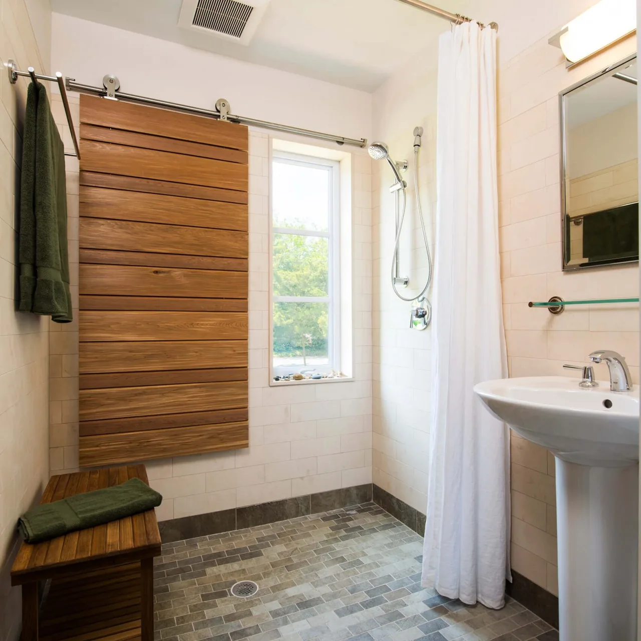 Bathroom with a tiled shower area, wooden sliding door, and pedestal sink under a mirror.