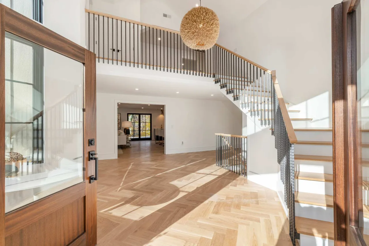 Entry area with herringbone wood flooring and staircase featuring black metal balustrade and natural wood handrails.