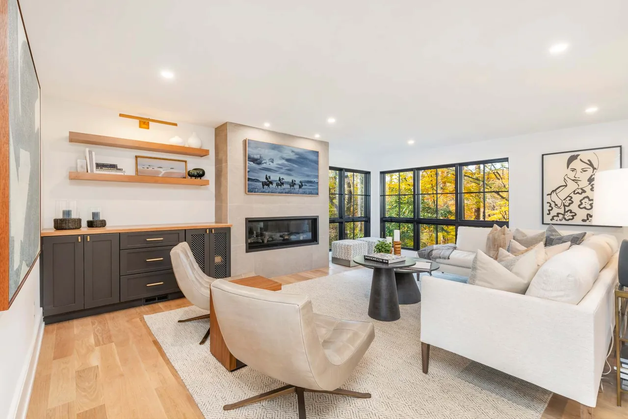 Living room in Parkside Sanctuary features floor-to-ceiling black wood-framed windows and a linear fireplace with stone surround.