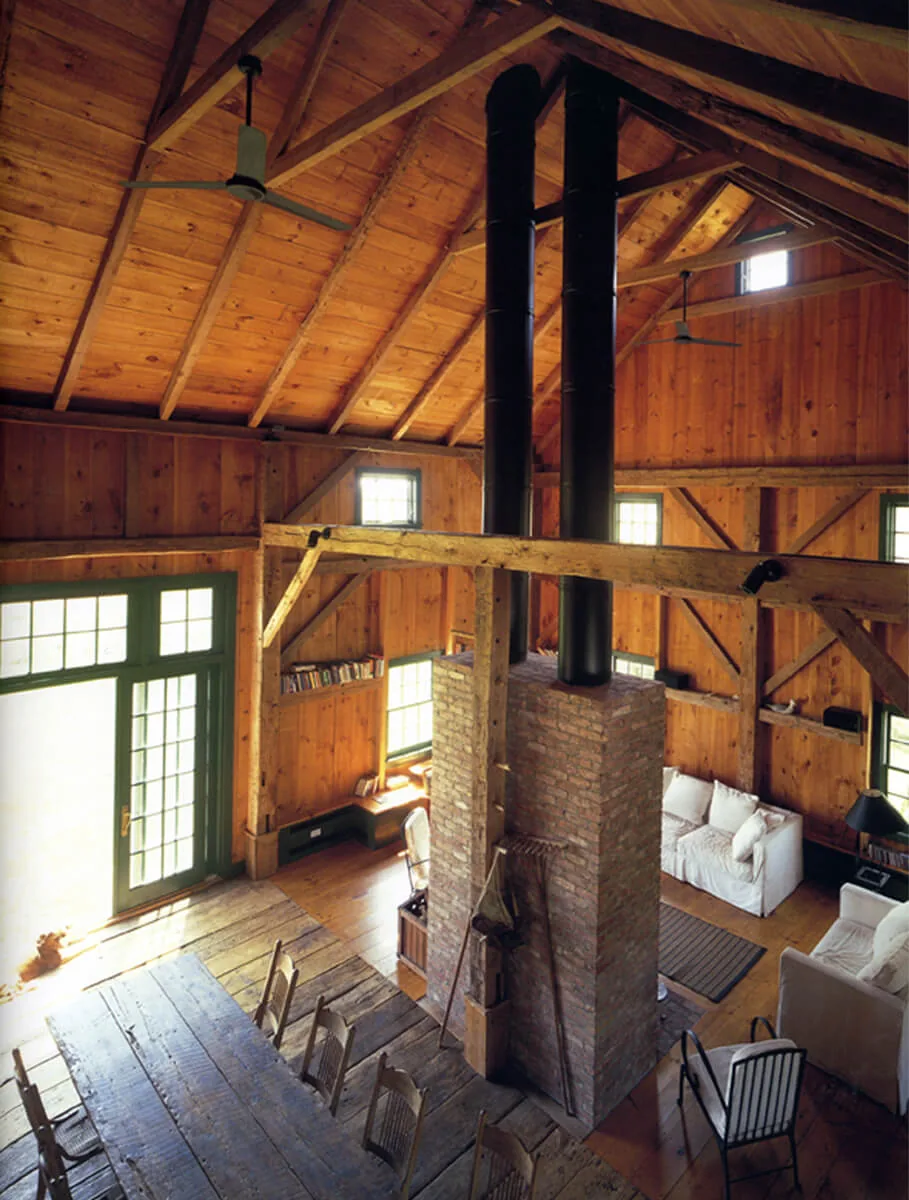 Living and dining area of Middleton-Waln Barn Home features exposed wooden beams and a central double brick chimney.