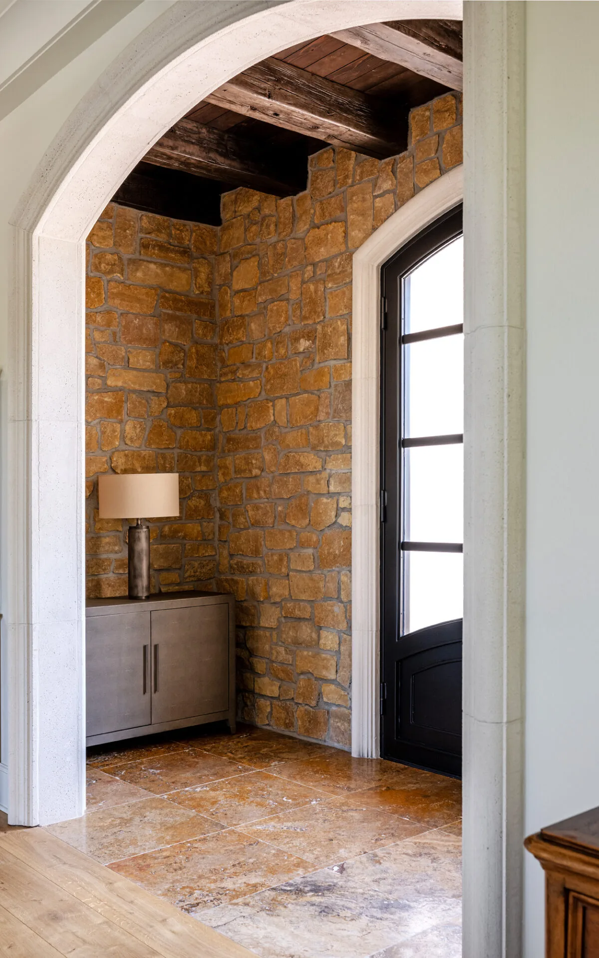 Entry area with brown stone walls, arched doorframe, and a black metal-framed door with glass panes.
