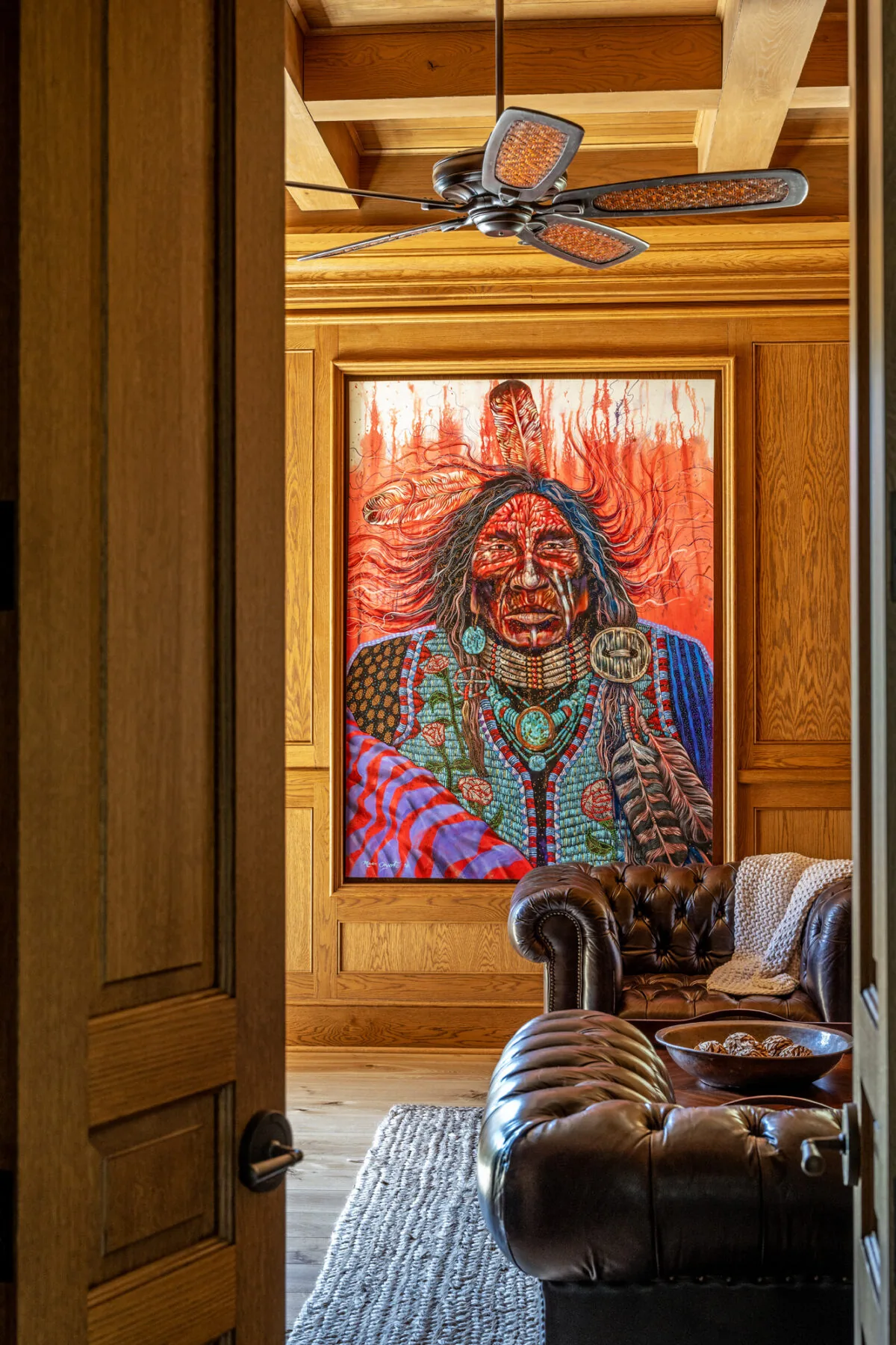 Living room with detailed wood paneling, a large vibrant Native American portrait, and tufted leather sofas.