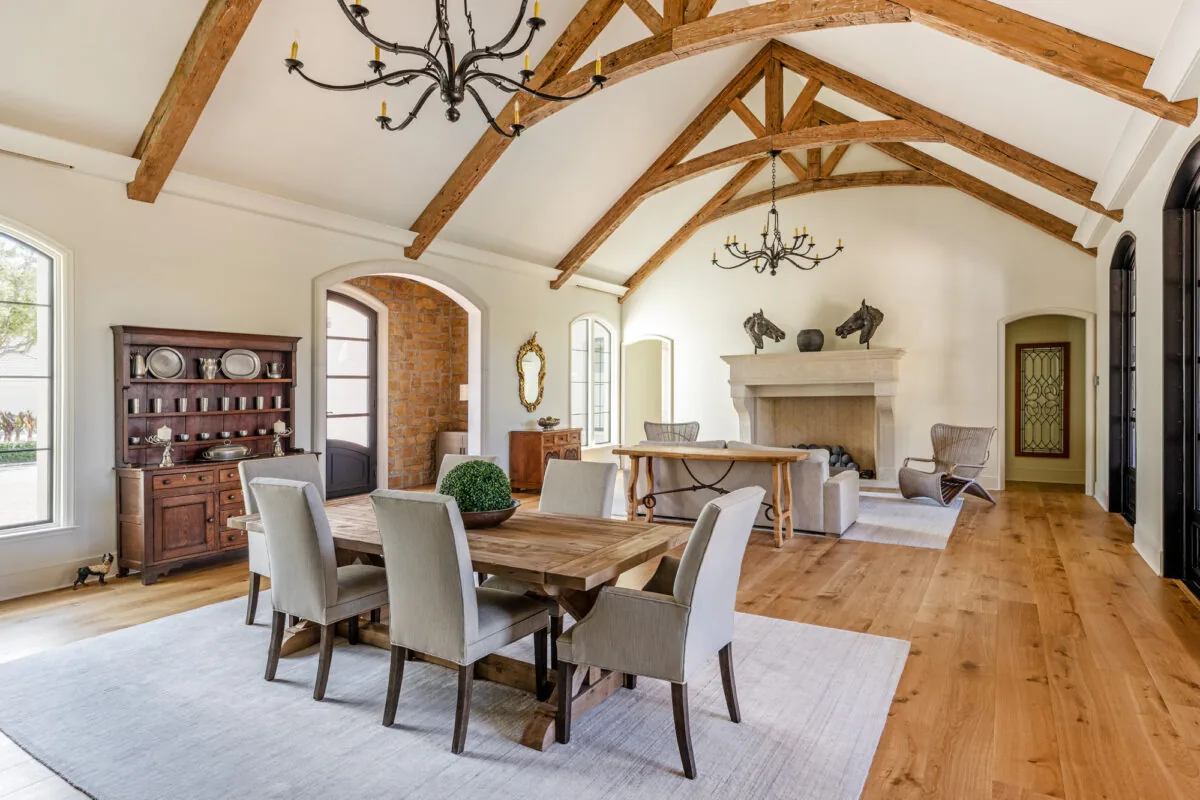 Living and dining room features exposed wood beams, vaulted ceiling, and a large stone fireplace in the French Countryside project.