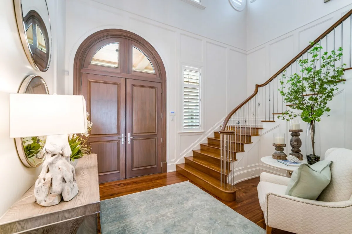 Entryway with arched double front doors, hardwood staircase, and white paneled walls.
