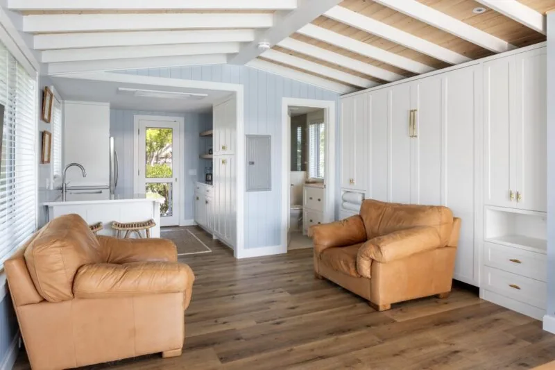 Interior view of Tide House living area with vaulted ceiling, white cabinetry, and adjacent kitchen space.