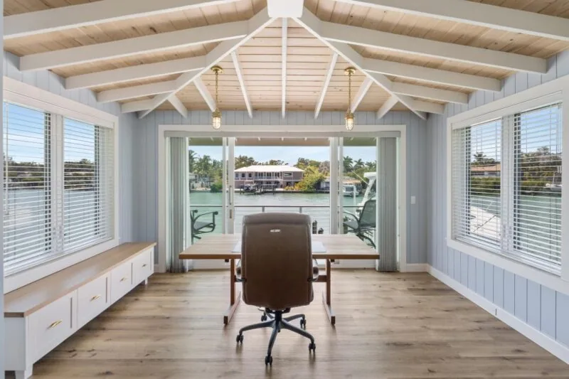 Tide House home office overlooks the waterfront through sliding glass doors and windows with white blinds.