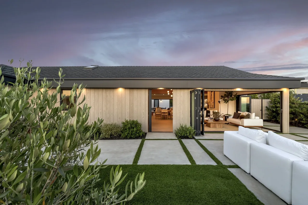 White Sails Residence features bi-fold black-framed glass doors connecting the living area to an outdoor patio with minimal landscaping.