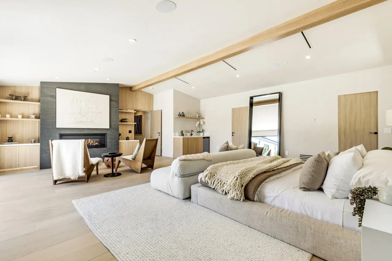 This bedroom includes a fireplace with black surround, built-in shelving, and a seating area with armchairs facing the fire.
